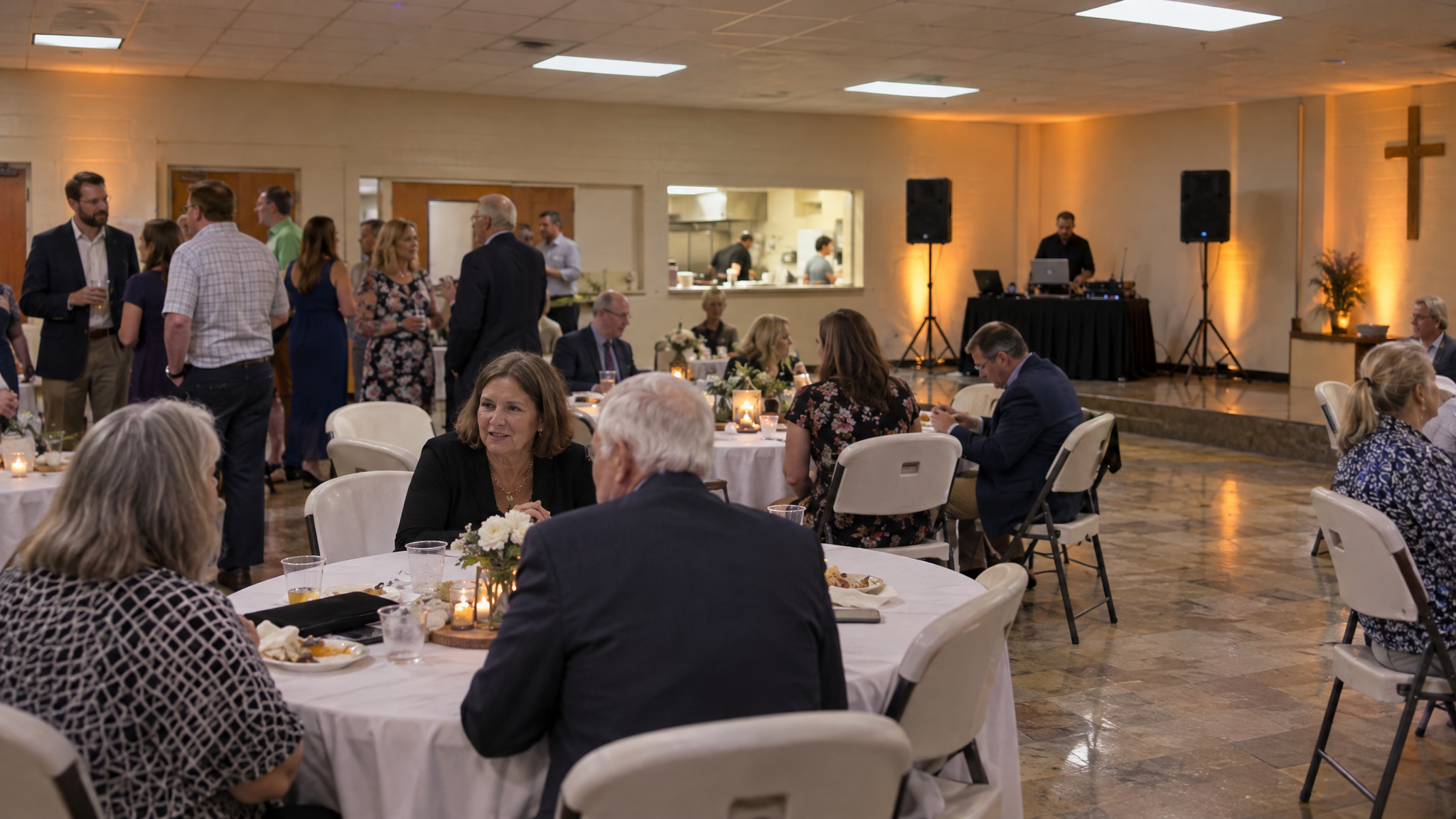 Church fellowship hall in Auburn Alabama set up for a fundraiser banquet with round tables, white tablecloths, DJ speakers, and warm uplighting on the walls